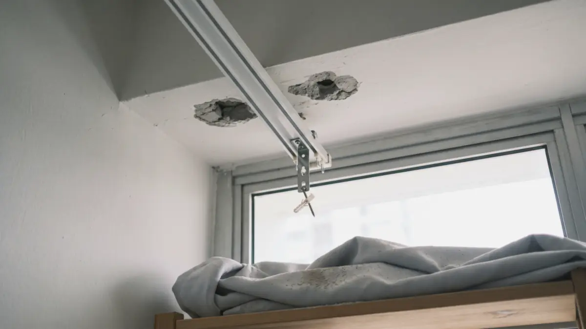 Curtain track hanging loose from an HDB ceiling beside two crumbled bracket holes