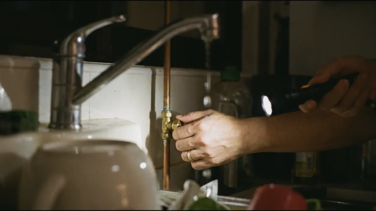 Hand closing the isolation valve under a sink while the tap drips
