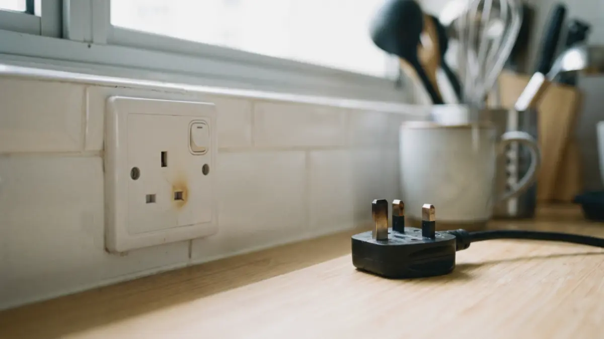 White wall socket with a brown scorch mark beside an unplugged 3-pin plug on a kitchen counter